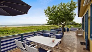 An outdoor patio with a table and chairs, a large umbrella, and a view of the beach and pier. - Skaerven Beachfront Condos and Cottage (Nyborg)