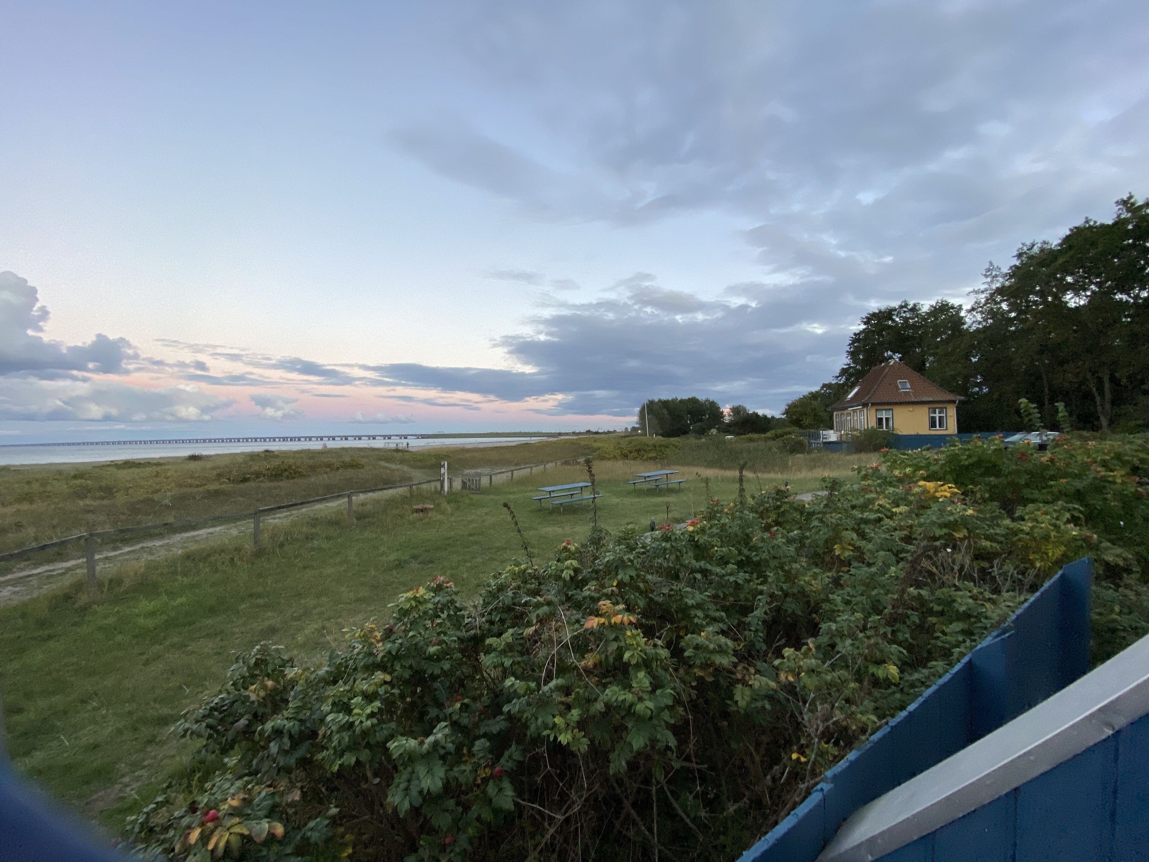 A coastal landscape with a house, grassy areas, and a pier extending into the water.