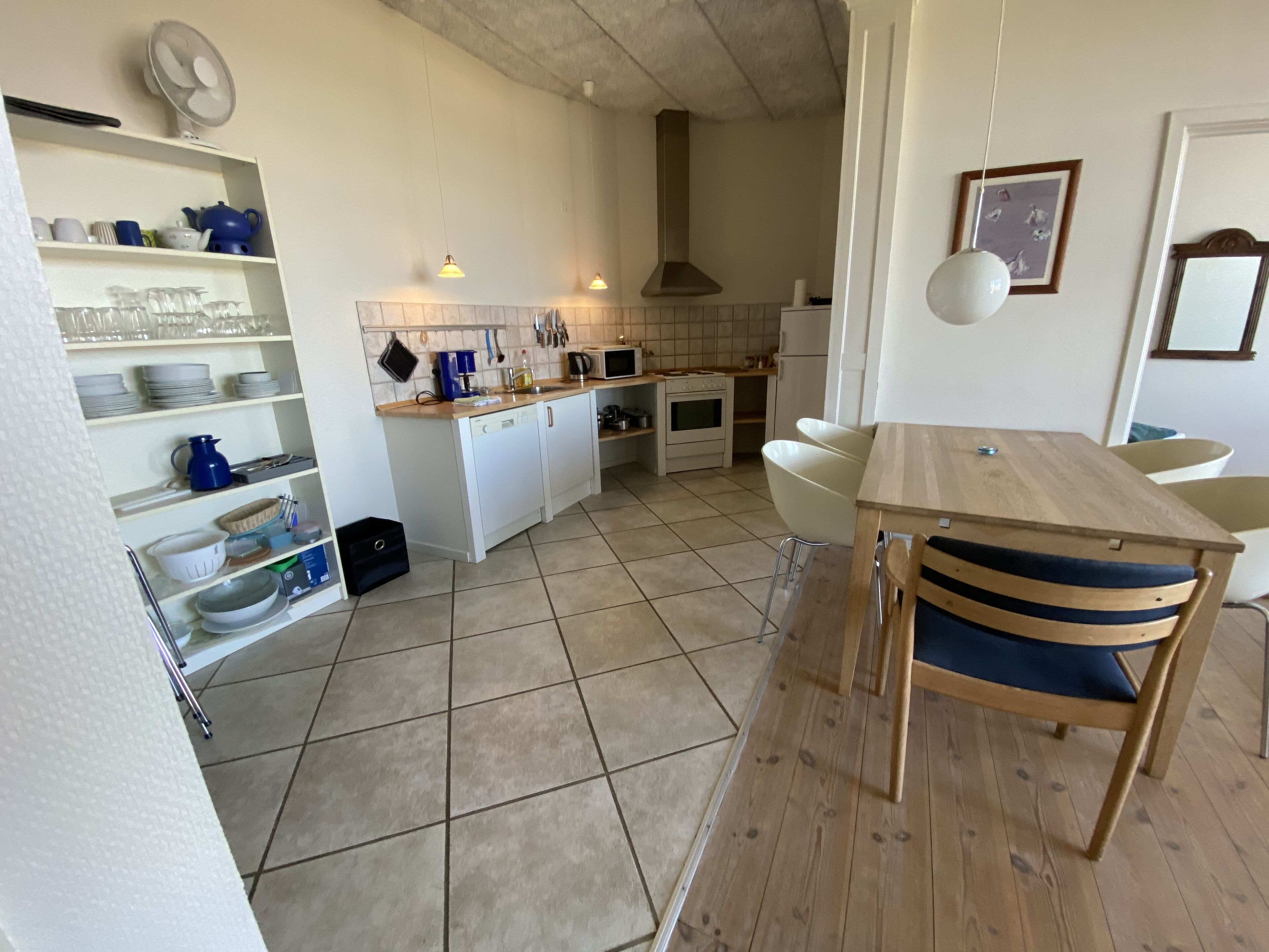 A compact kitchen with white cabinets, a wooden dining table, and a tiled floor.