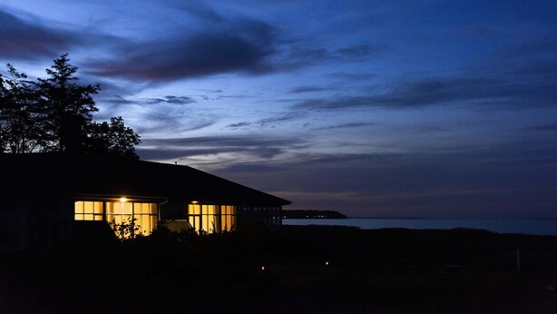 A house with large windows and a view of the sea at dusk. - Skaerven Beachfront Condos and Cottage (Nyborg)