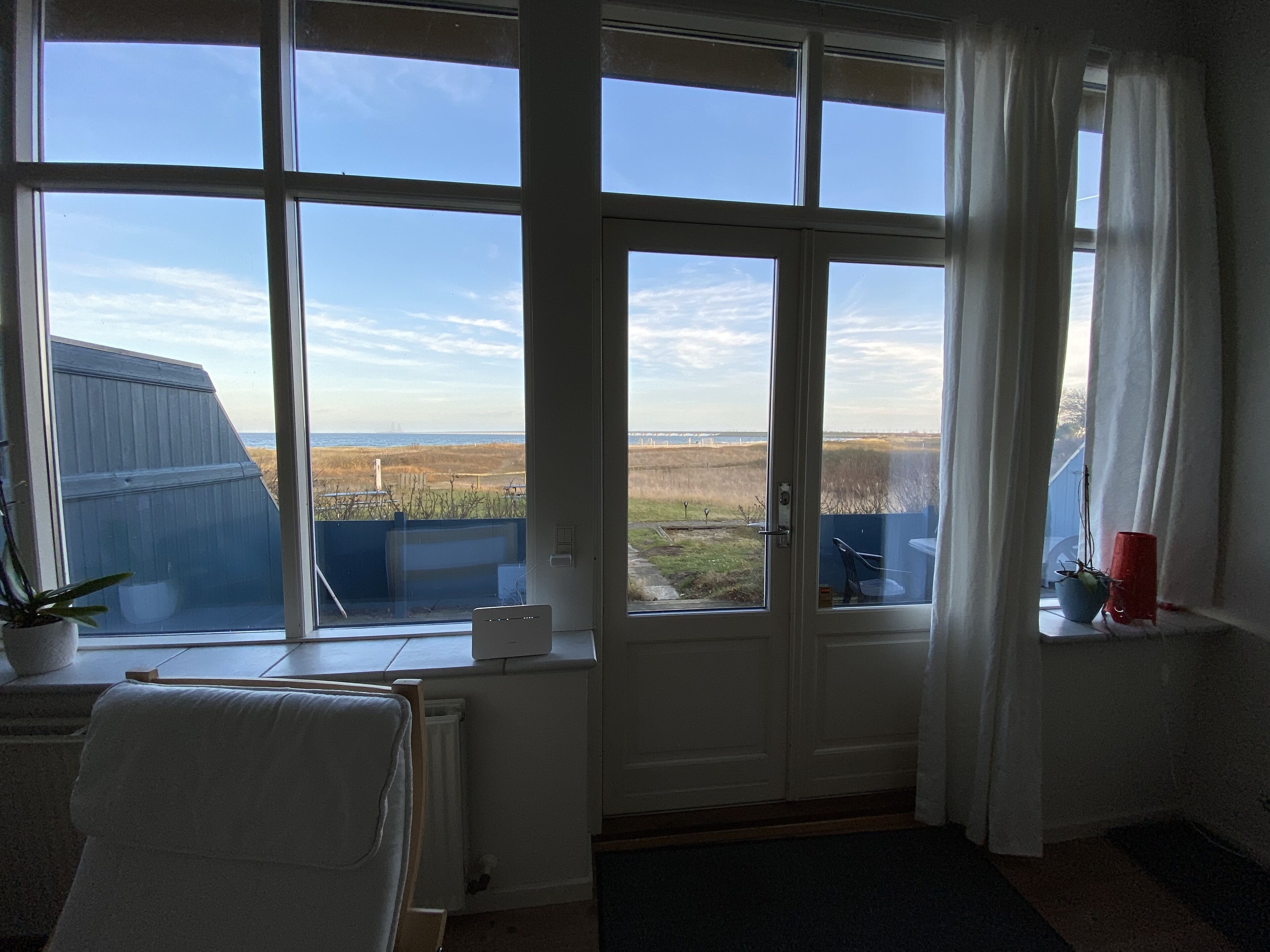 A room with large windows offering a view of a coastal landscape, a radiator, and a chair.