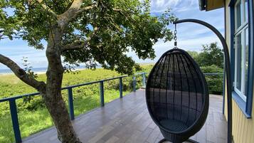 A wooden deck with a hanging chair, a tree, and a view of the landscape.