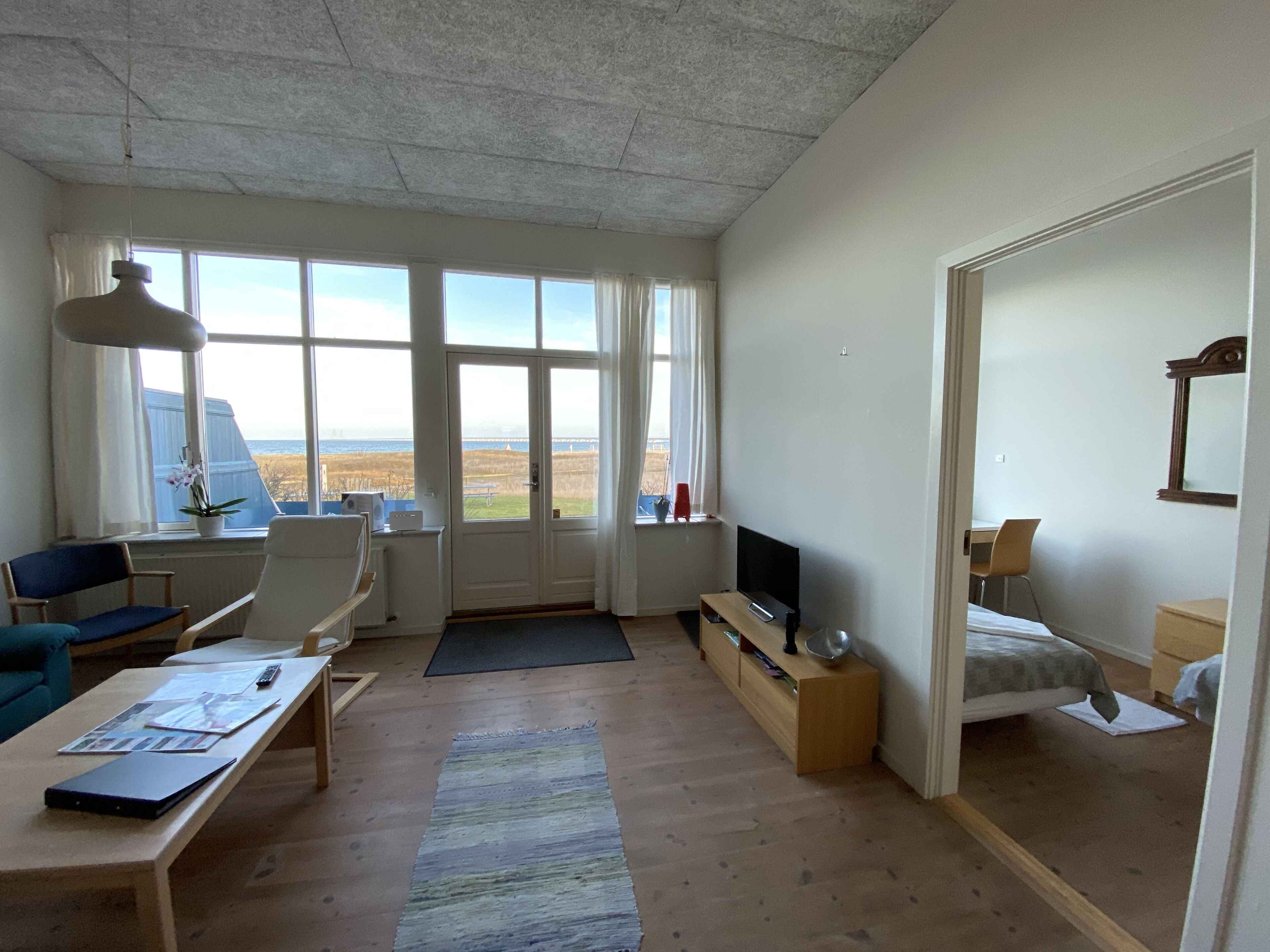 A modern living room with a large window, a flat-screen TV, a sofa, a coffee table, and a bed.