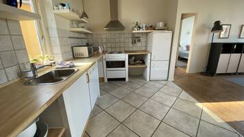 Een keuken met witte kastjes, een fornuis, een spoelbak en een koelkast.