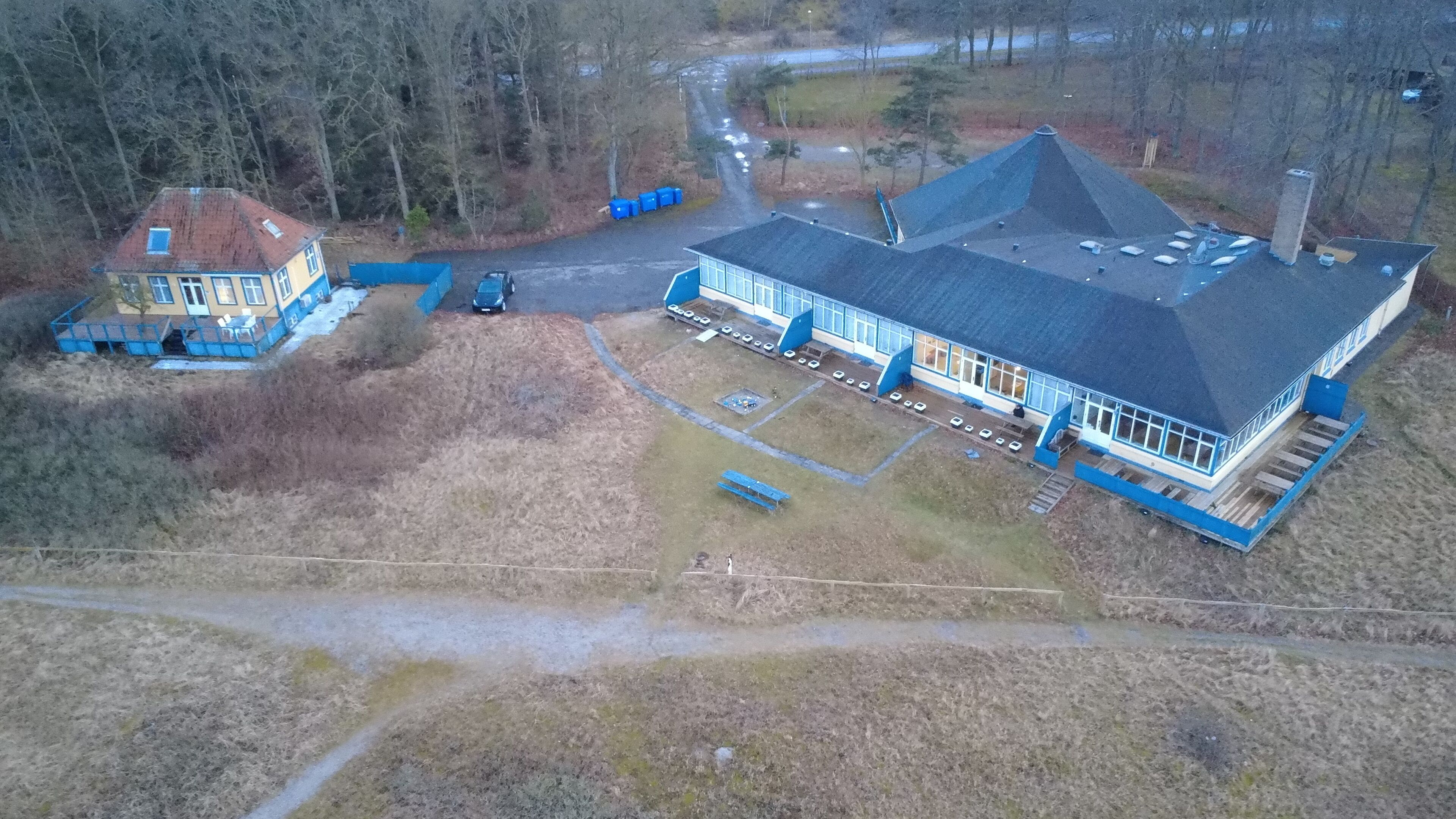 Luchtbeeld van een groot gebouw met een steil dak, omringd door een parkeerplaats en een kleine tuin.