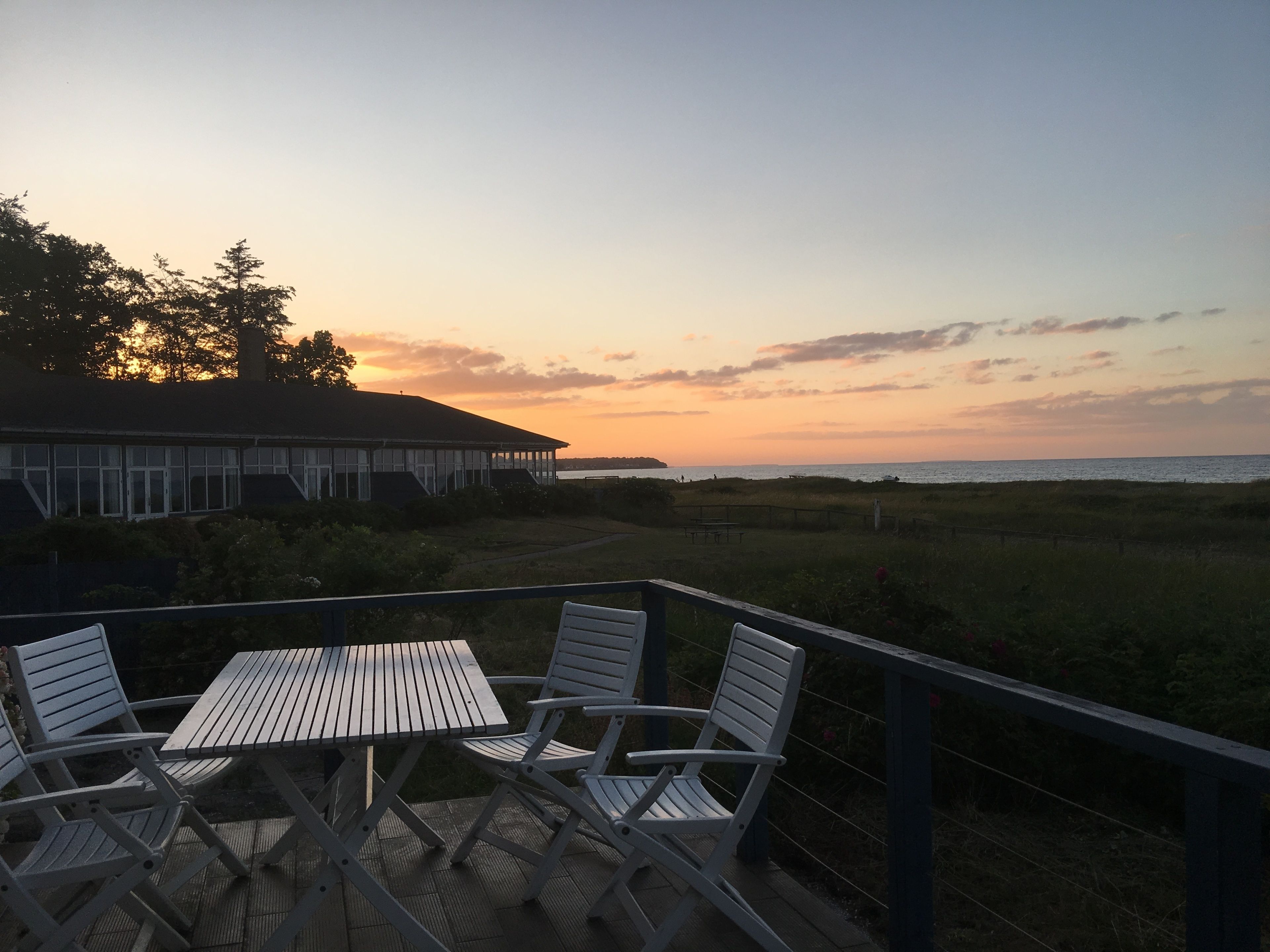 A deck with a table and chairs overlooking a beach at sunset.
