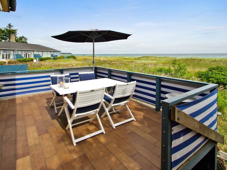 A deck with a table and chairs, an umbrella, and a view of the beach.