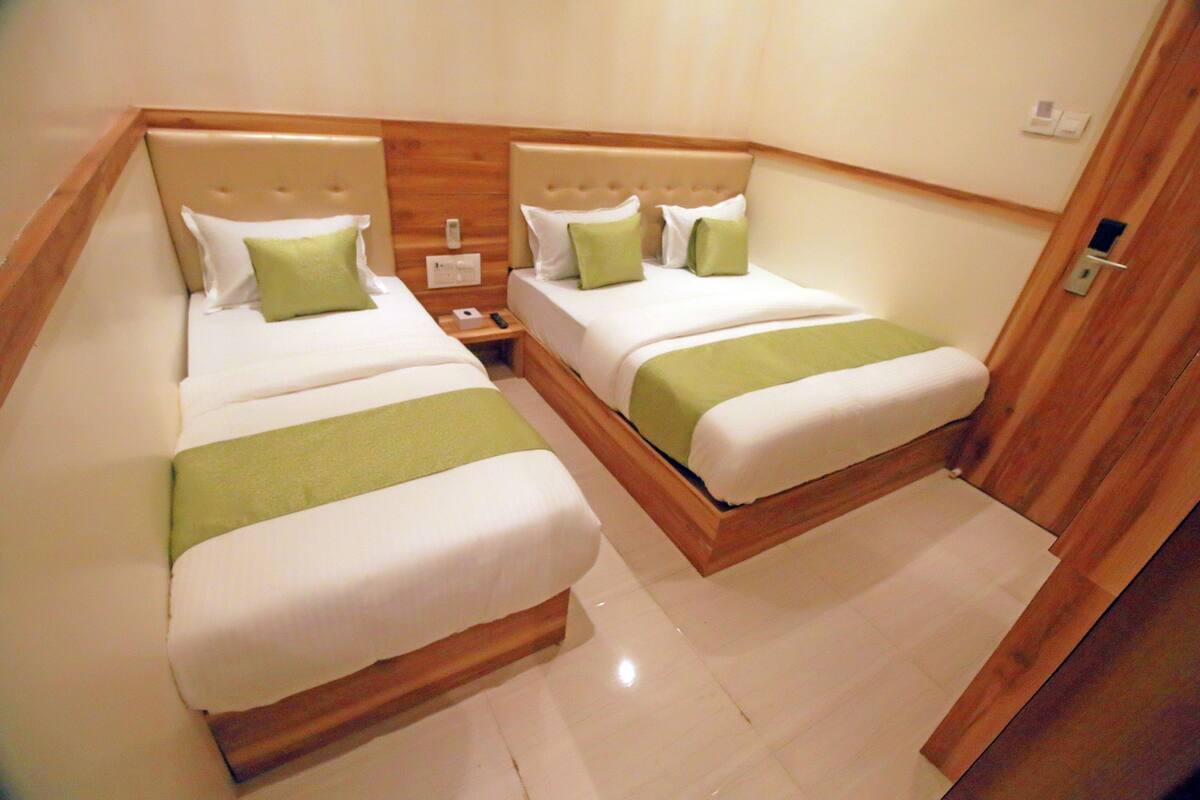 A hotel room with two beds, each with a green bedspread and white pillows.