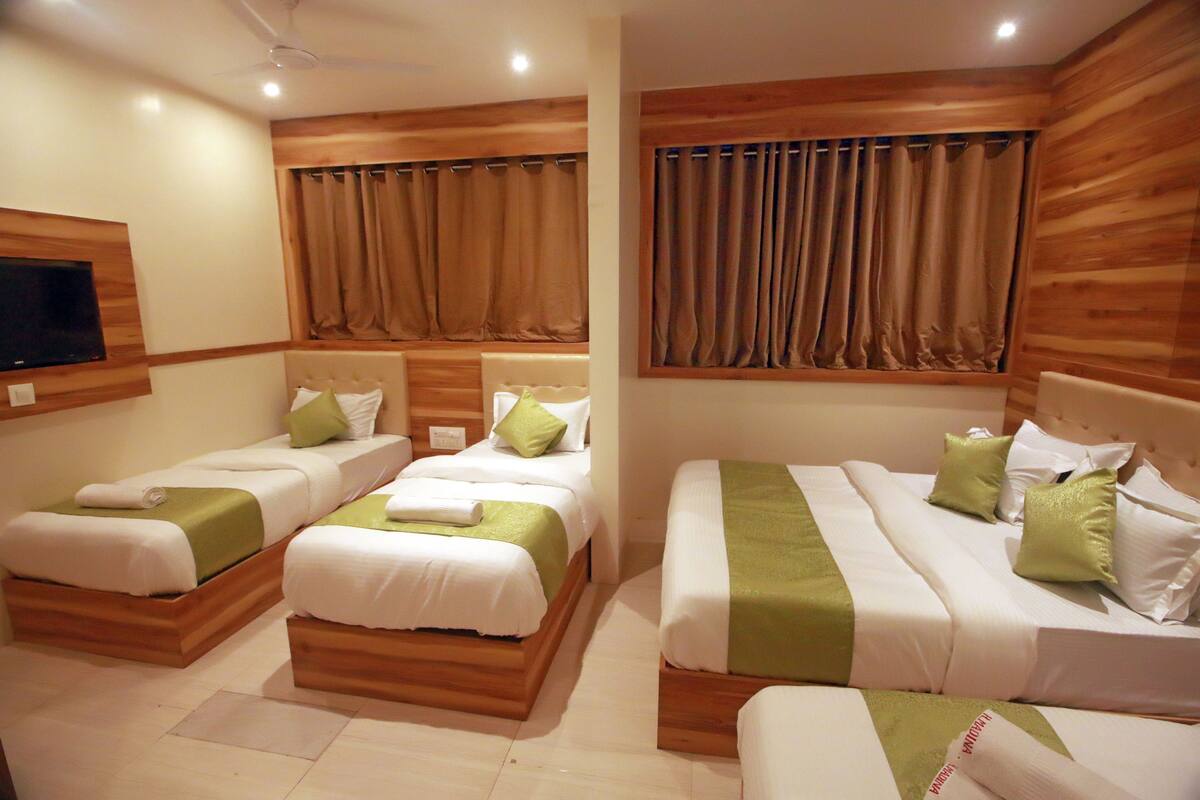 A hotel room with three beds, wooden headboards, a flat-screen TV, and curtains.