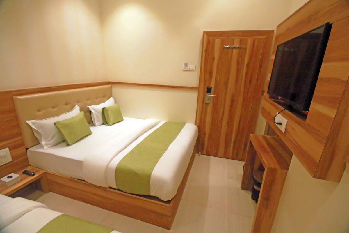 A hotel room with a bed, a TV mounted on the wall, and a wooden door.
