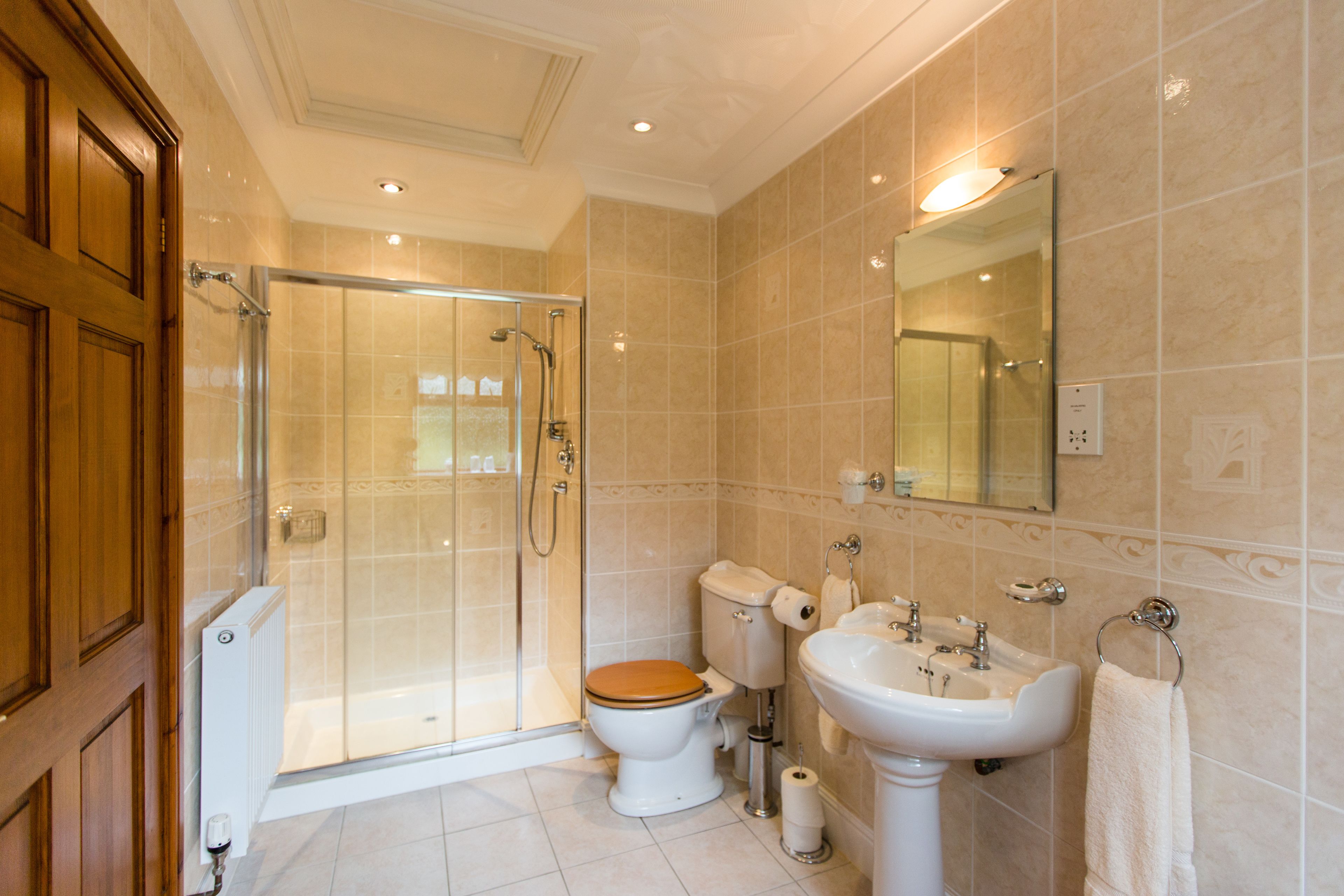A bathroom with a glass-enclosed shower, a toilet with a wooden seat, and a pedestal sink.
