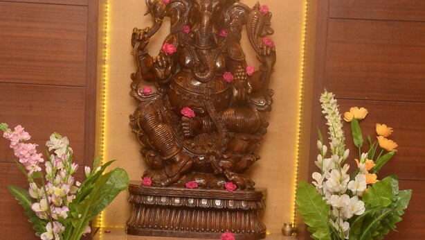 A wooden shrine with an ornate statue, two flower arrangements, and a brass bowl with pink flower petals.