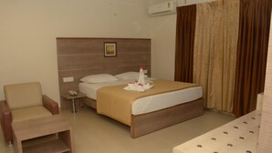 A hotel room with a bed, a chair, a bedside table, and an air conditioning unit.