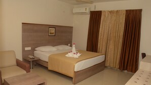 A hotel room with a bed, a chair, a small table, an air conditioning unit, and a curtain.