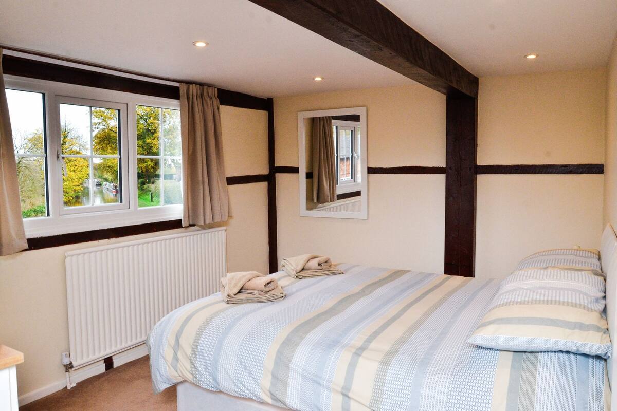 A bedroom with a large bed, a window with curtains, a radiator, and a mirror on the wall.