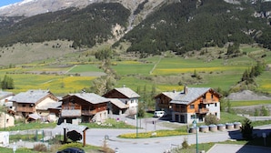 A mountain village with traditional wooden houses, a paved road, and a clear view of snow-capped mountains. - Cozy 4 pers. apt at the slopes with parking and pool - Lanslebourg (Lanslebourg-Mont-Cenis)