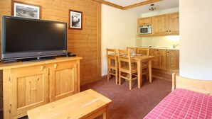 A compact room with a wooden TV stand, a dining table with chairs, a small kitchen area with a microwave, and a bed with a red checkered bedspread. - Cozy 4 pers. apt at the slopes with parking and pool - Lanslebourg (Lanslebourg-Mont-Cenis)
