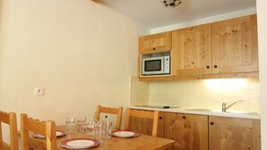 A compact kitchen with wooden cabinets, a microwave, and a dining table set for four. - Cozy 4 pers. apt at the slopes with parking and pool - Lanslebourg (Lanslebourg-Mont-Cenis)