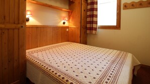 A wooden room with a bed, two wall-mounted lamps, a window with a plaid curtain, and a wooden headboard. - Cozy 4 pers. apt at the slopes with parking and pool - Lanslebourg (Lanslebourg-Mont-Cenis)