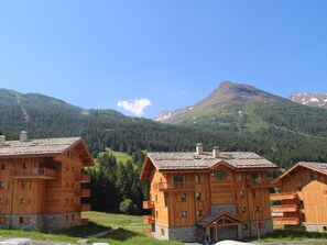 A wooden chalet-style building with multiple balconies and a stone foundation, surrounded by a mountainous landscape.