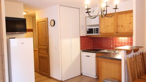 A compact kitchen with a refrigerator, microwave, stove, and wooden cabinets. - Spacious apartment in Lanslevillard with balcony and parking (Lanslevillard)