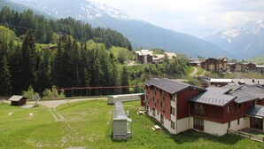 A mountainous village with traditional buildings, a small lodge, and a clear view of the surrounding peaks. - Val Cenis Le Haut: Cozy Studio for 3 near Slopes & Amenities, Ski Locker Included (Lanslevillard)