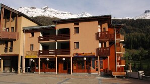 A multi-story building with balconies and a sign indicating a location for rentals. - Val Cenis Le Haut: Cozy Studio for 3 near Slopes & Amenities, Ski Locker Included (Lanslevillard)