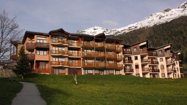 A multi-story hotel with balconies, a paved path, and a mountainous backdrop. - Val Cenis Le Haut: Cozy Studio for 3 near Slopes & Amenities, Ski Locker Included (Lanslevillard)