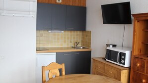 A compact kitchen with a wooden table, a microwave, and a TV mounted on the wall. - Val Cenis Le Haut: Cozy Studio for 3 near Slopes & Amenities, Ski Locker Included (Lanslevillard)