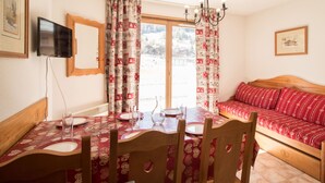 Un coin repas avec une table dressée pour quatre personnes, un canapé, un téléviseur fixé au mur et une fenêtre avec des rideaux.