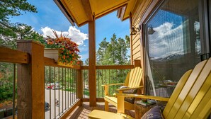 Un pontile in legno con una sedia Adirondack gialla, un vaso di fiori appeso e vista su una strada e alberi.