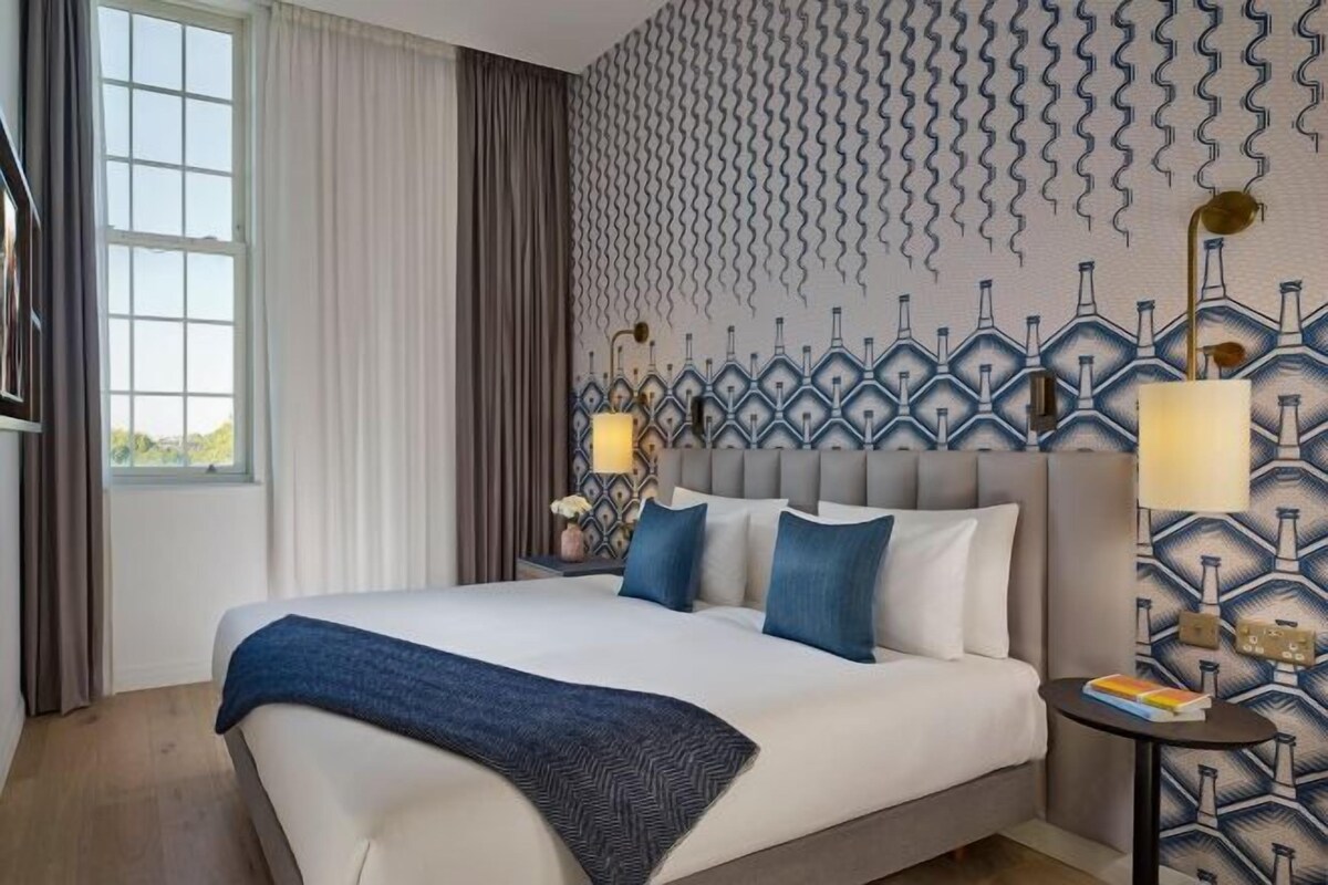 A hotel room with a large bed, a nightstand, a lamp, and a patterned wall.