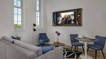A modern living room with a grey sofa, blue chairs, a round dining table, and a mounted TV.