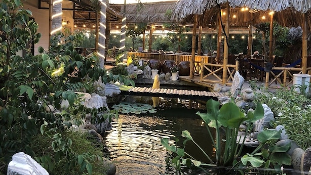 A tranquil garden with a pond, a wooden bridge, and bamboo structures. - Homestay Songngu Pisces (Can Tho)