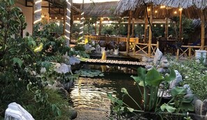 A tranquil garden with a pond, a wooden bridge, and bamboo structures. - Homestay Songngu Pisces (Can Tho)