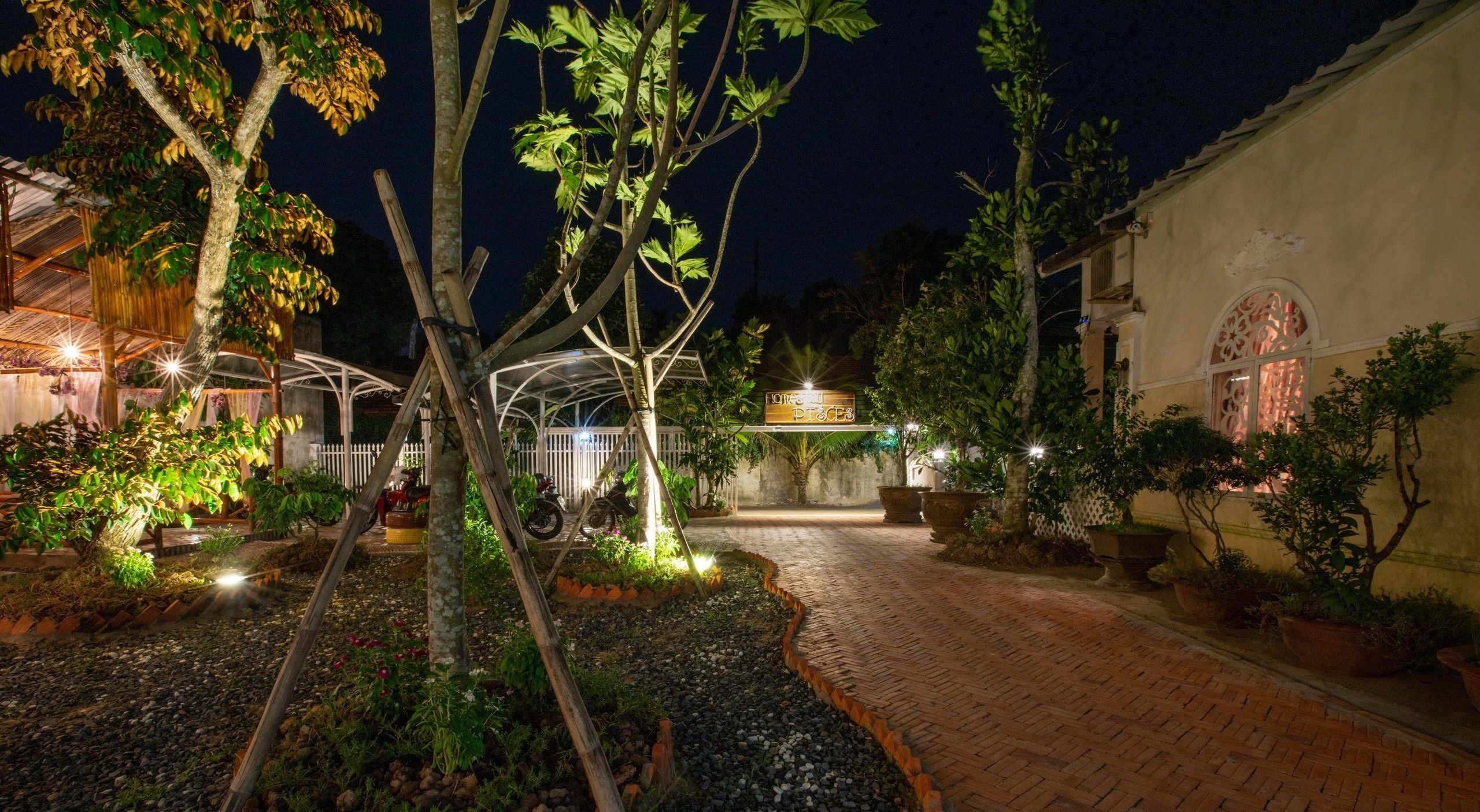 A nighttime view of a garden area with a pathway leading to a building with a sign reading "Home & Pieces."