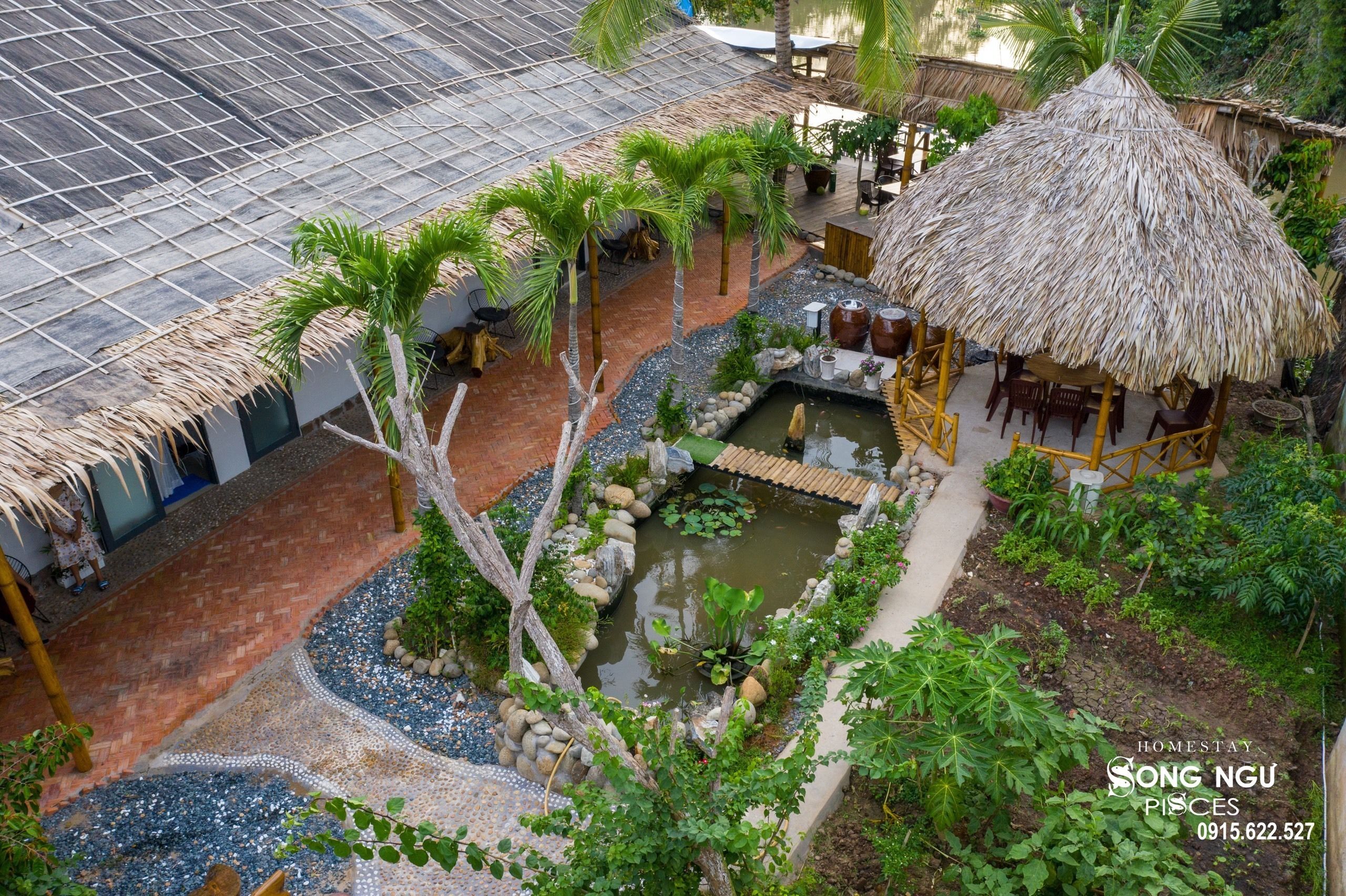 Un jardín tropical con un estanque, palmeras y una cabaña con techo de paja.