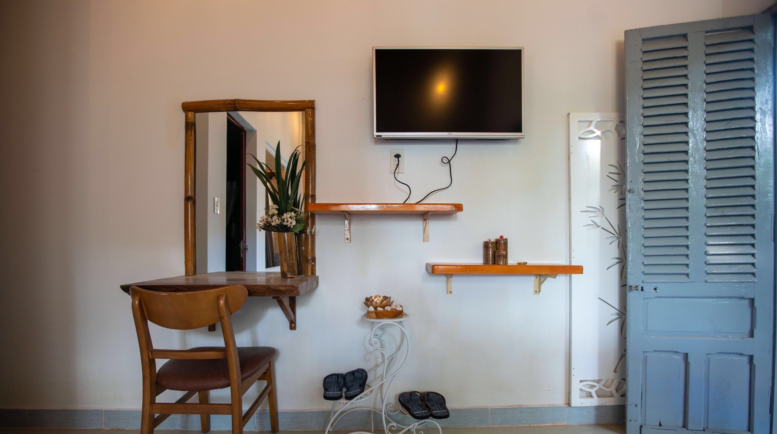 Una stanza con una sedia in legno, uno specchio, una TV montata a parete e una porta con persiane.