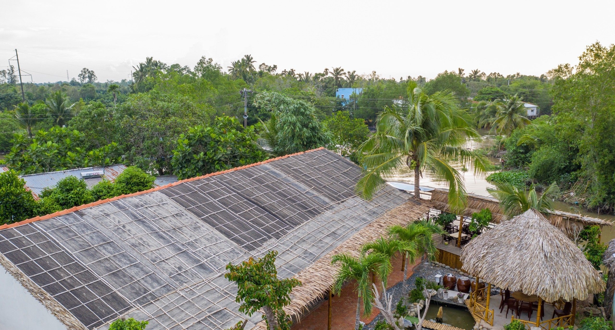 A rooftop with a grid of solar panels, surrounded by lush greenery and a thatched-roof structure.