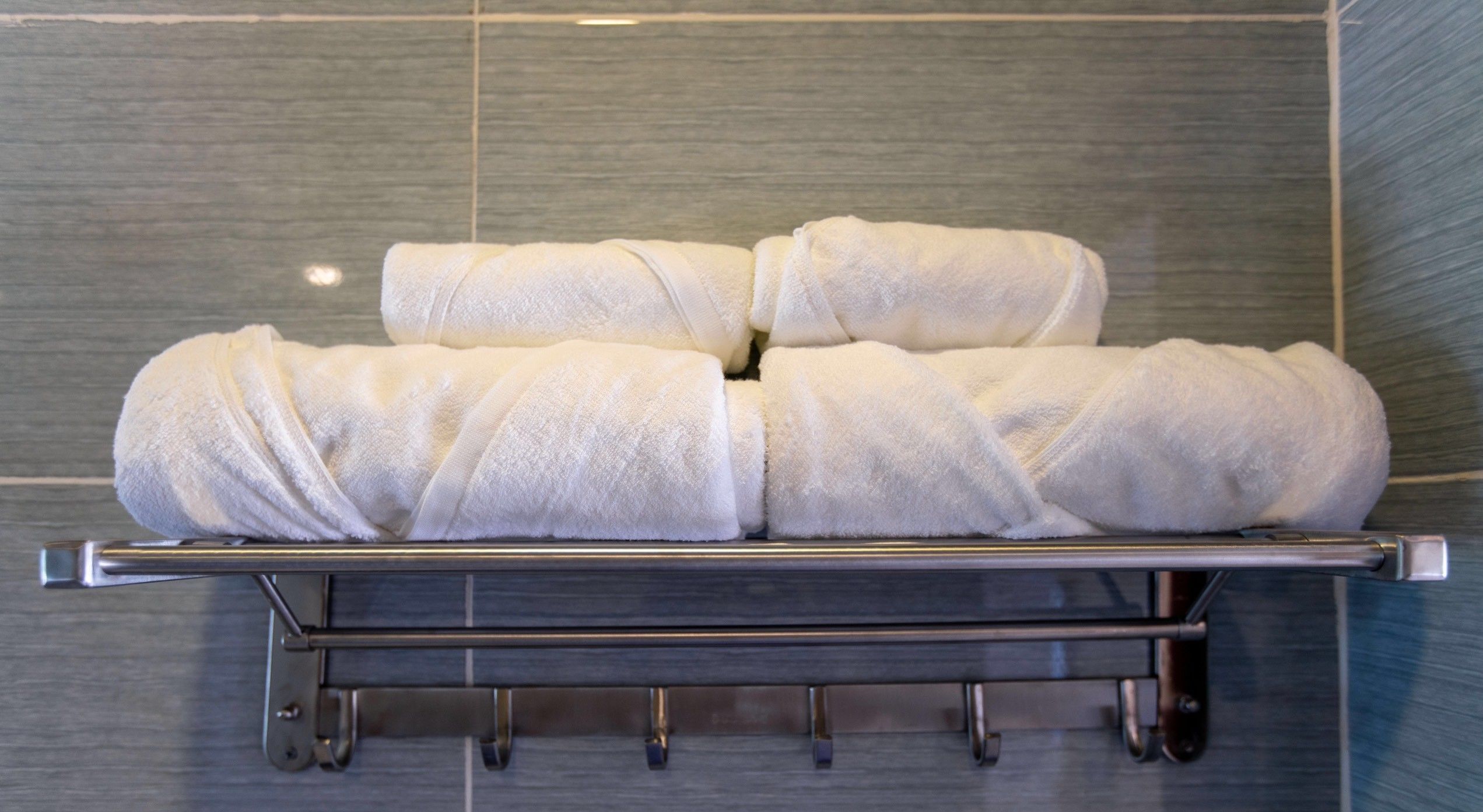 A metal towel rack with four neatly folded white towels against a tiled wall.