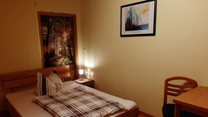 Ein Hotelzimmer mit Bett, Nachttisch mit Lampe, Holzstuhl und einem Gemälde an der Wand.