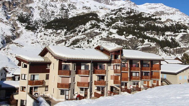 A multi-story hotel with balconies, set against a backdrop of snow-covered mountains. - Apartment for 4 in "Les Hauts de Val Cenis" – Ski-in/Ski-out, Near ESF & Shops (Lanslevillard)