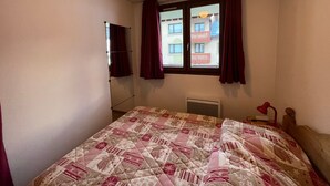 A bedroom with a bed, a window with curtains, a radiator, and a wall-mounted mirror. - Apartment in Lanslebourg Village, Val Cenis - 300m from Ski Slopes (Lanslebourg-Mont-Cenis)