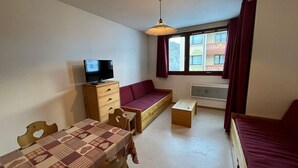 A compact room with a sofa, a television on a wooden cabinet, a dining table with a patterned tablecloth, and a window with curtains. - Apartment in Lanslebourg Village, Val Cenis - 300m from Ski Slopes (Lanslebourg-Mont-Cenis)