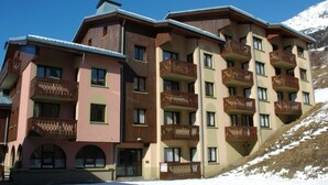 A multi-story hotel with balconies, a ski slope in the background, and a clear sky. - Apartment in Lanslebourg Village, Val Cenis - 300m from Ski Slopes (Lanslebourg-Mont-Cenis)