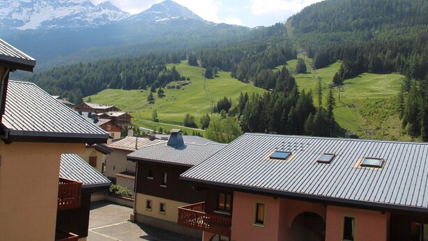 A mountain village with traditional buildings, a clear view of the surrounding hills and mountains, and a small parking area in the foreground. - Apartment in Lanslebourg Village, Val Cenis - 300m from Ski Slopes (Lanslebourg-Mont-Cenis)