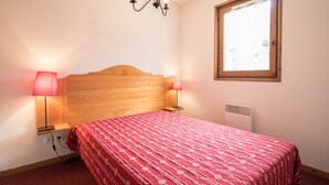 A bedroom with a wooden headboard, two bedside lamps, a radiator, and a window with a view. - Spacious apartment for 6, south balcony, parking (Lanslevillard)