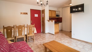 A living room with a red door, wooden furniture, a chandelier, and a TV mounted on the wall. - Spacious apartment for 6, south balcony, parking (Lanslevillard)