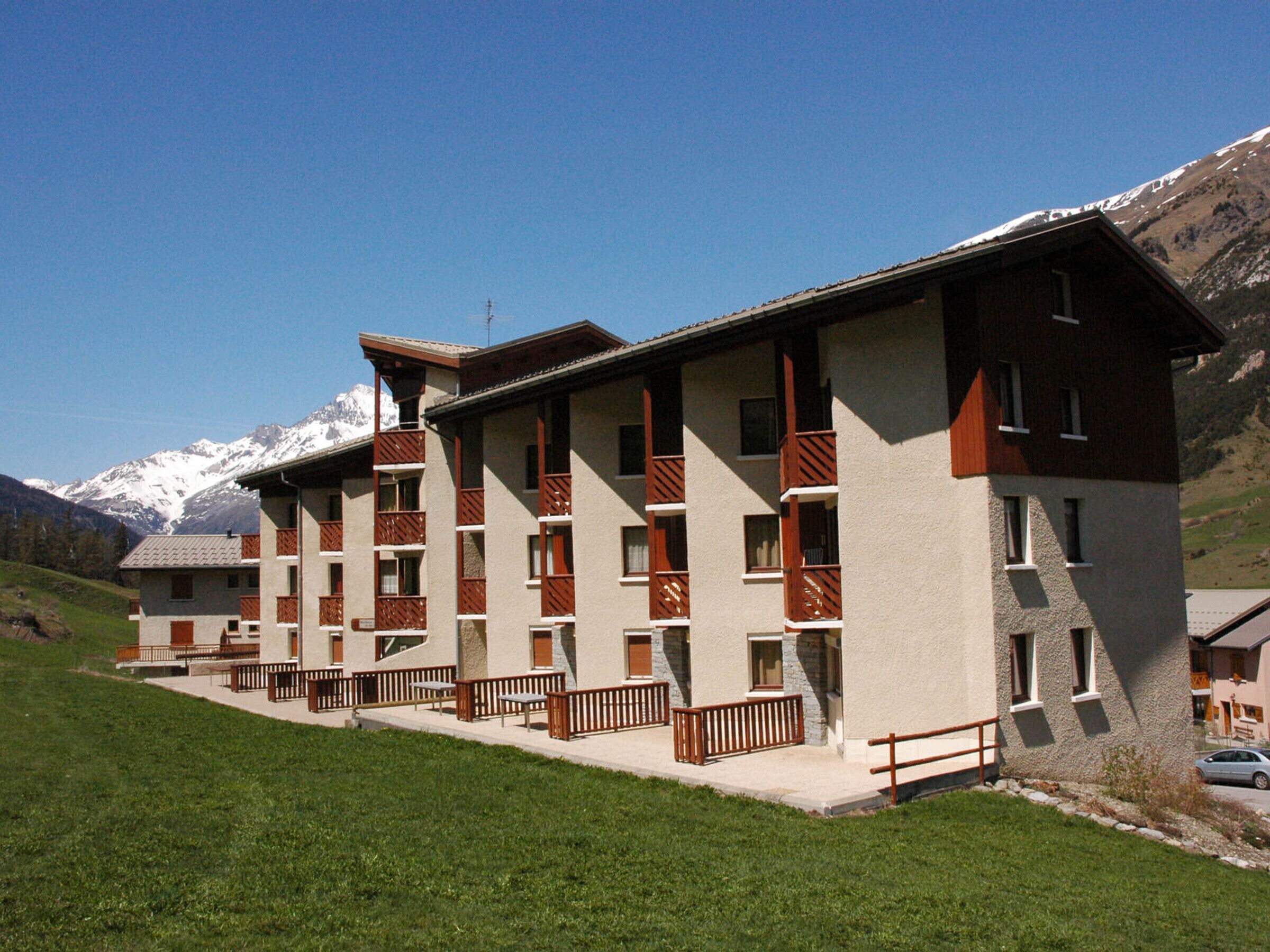 Un hotel de varios pisos con balcones, con montañas nevadas como telón de fondo.
