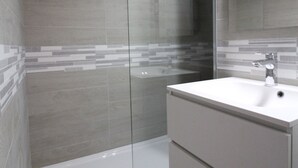 A modern bathroom with a glass shower enclosure, a white sink, and a tiled backsplash.